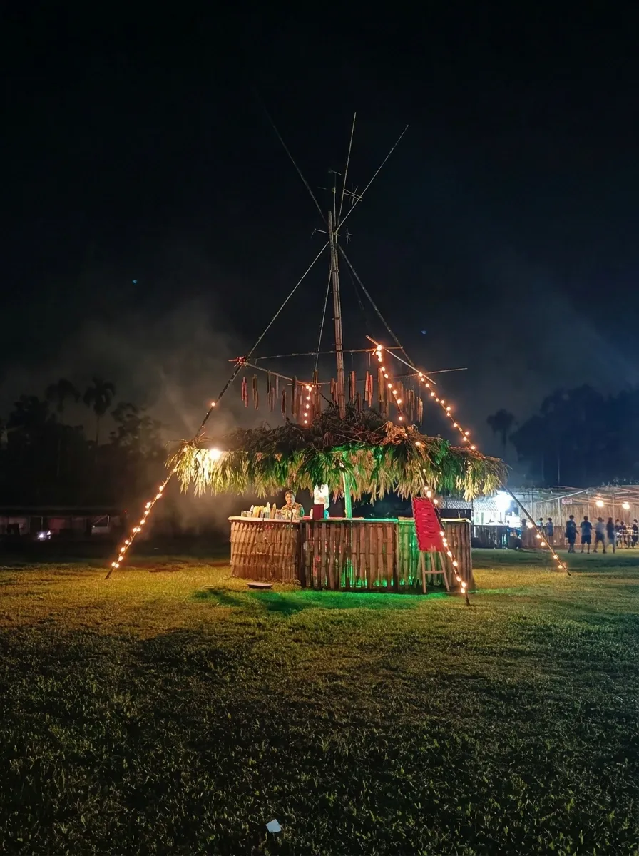 The central bamboo bar installation lit at night, string lights strung from its bamboo frame